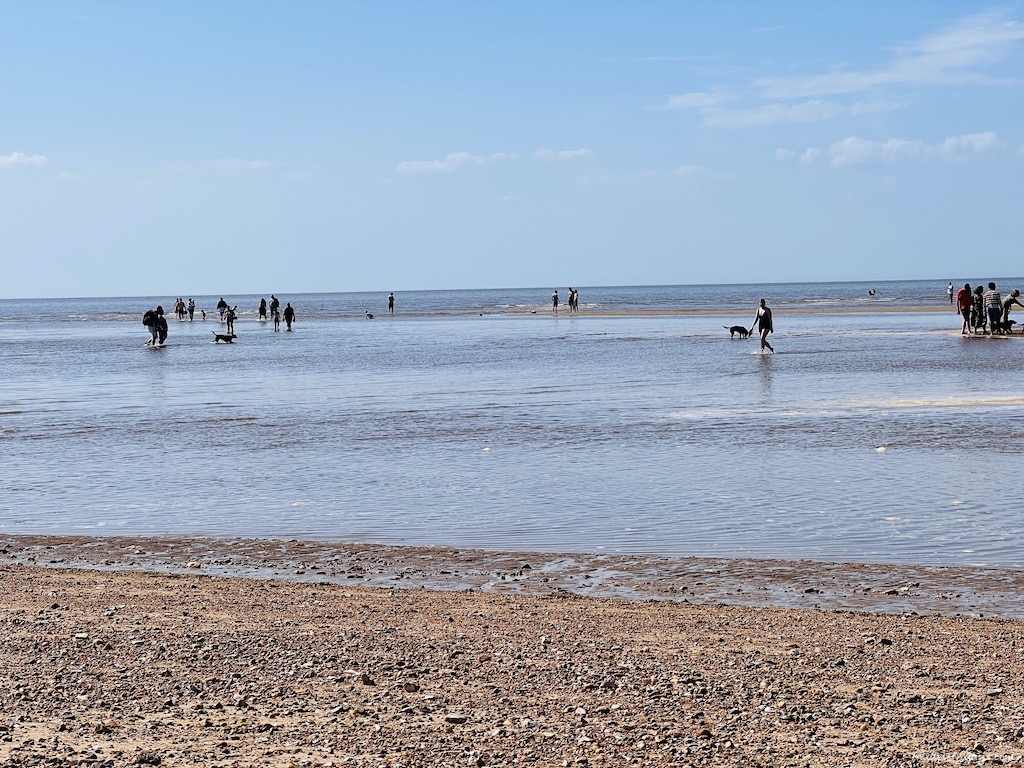 The tide coming in quickly  with people paddling in the sea