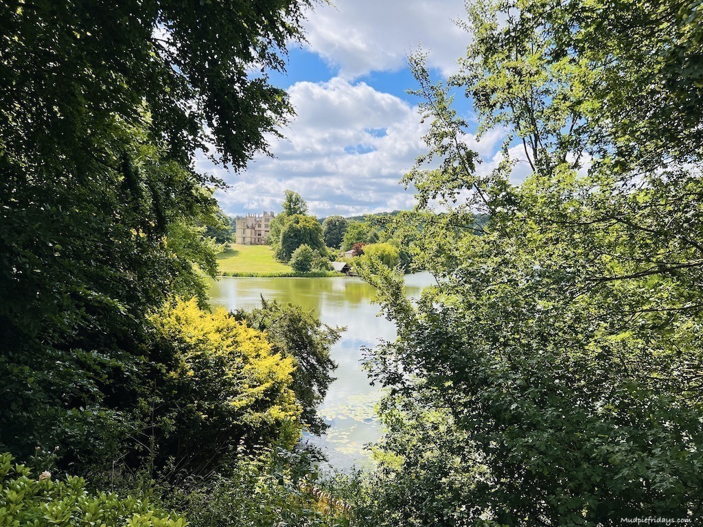 The view of new sherborne castle from across the lake with bushes and flowers