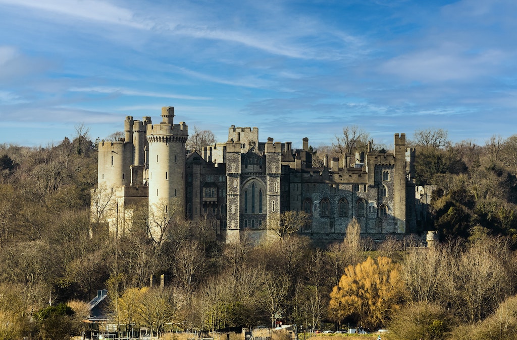 Arundel castle from afar in the sunshine with the trees surrounding it and blue sky 