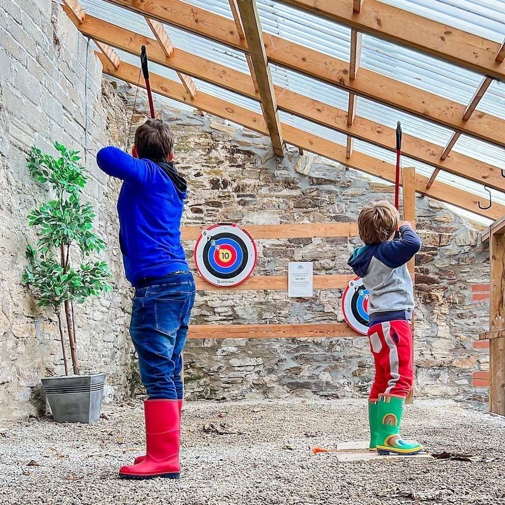 The boys playing archery in the archery barn at Glynn Barton Cottages Farm Stay in Cornwall