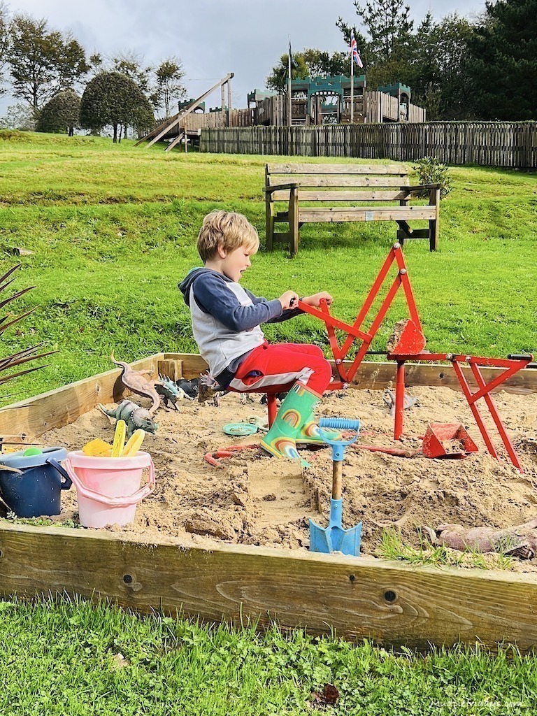 Harry in the sandpit sitting on diggers and digging the sand