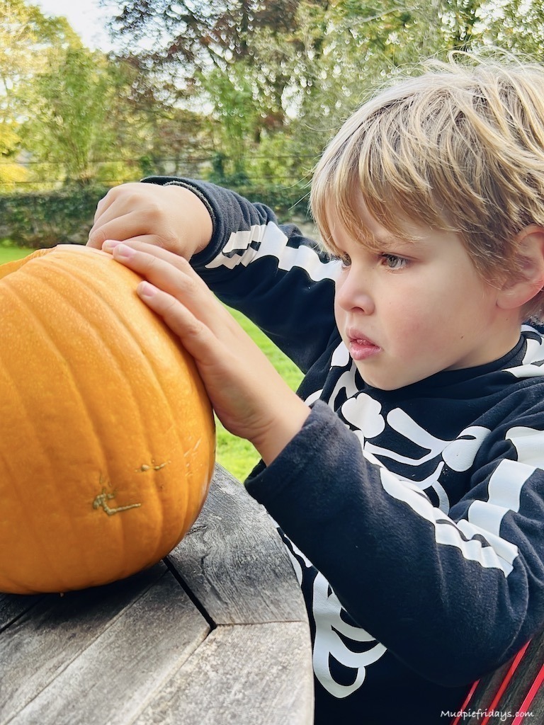 Harry carving a pumpkin on a wooden table in his Halloween Skeleton outfit