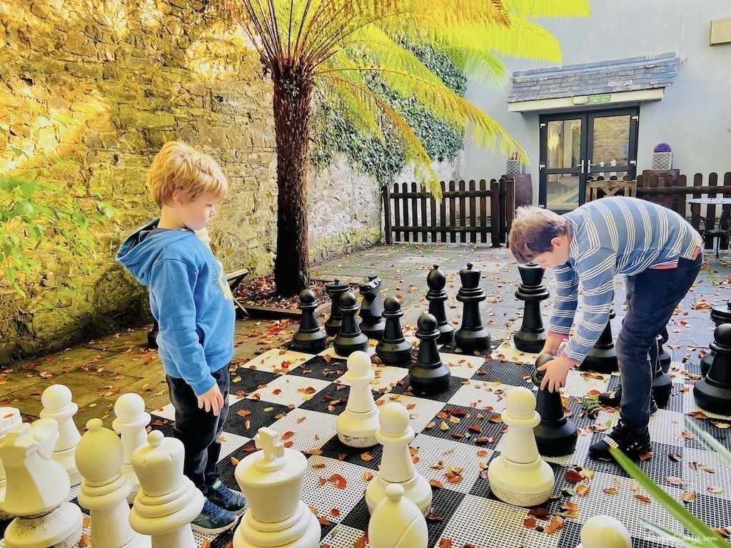 The boys playing a giant chess set underneath a tree fern at Glynn Barton Cottages a Cornwall family holiday