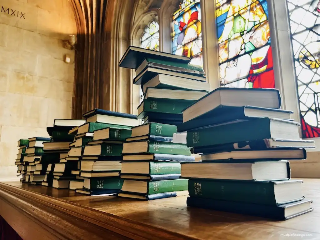 Stacks of prayer books and bibles with the stained glass window behind