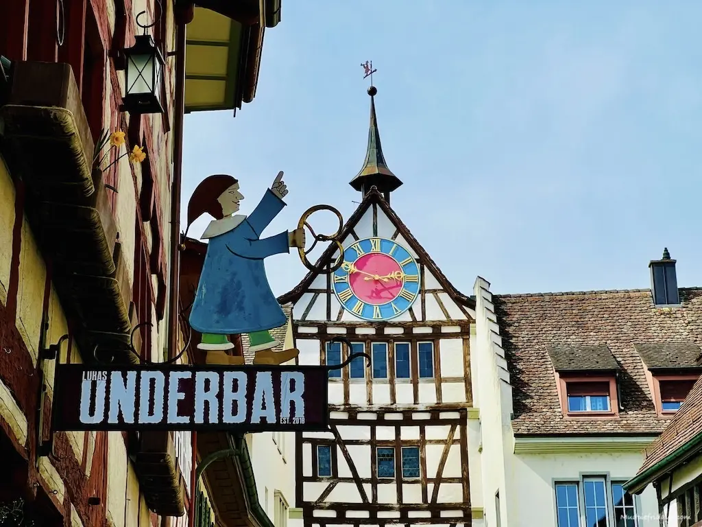 one of the street signs with the town clock in the background which is on the gate