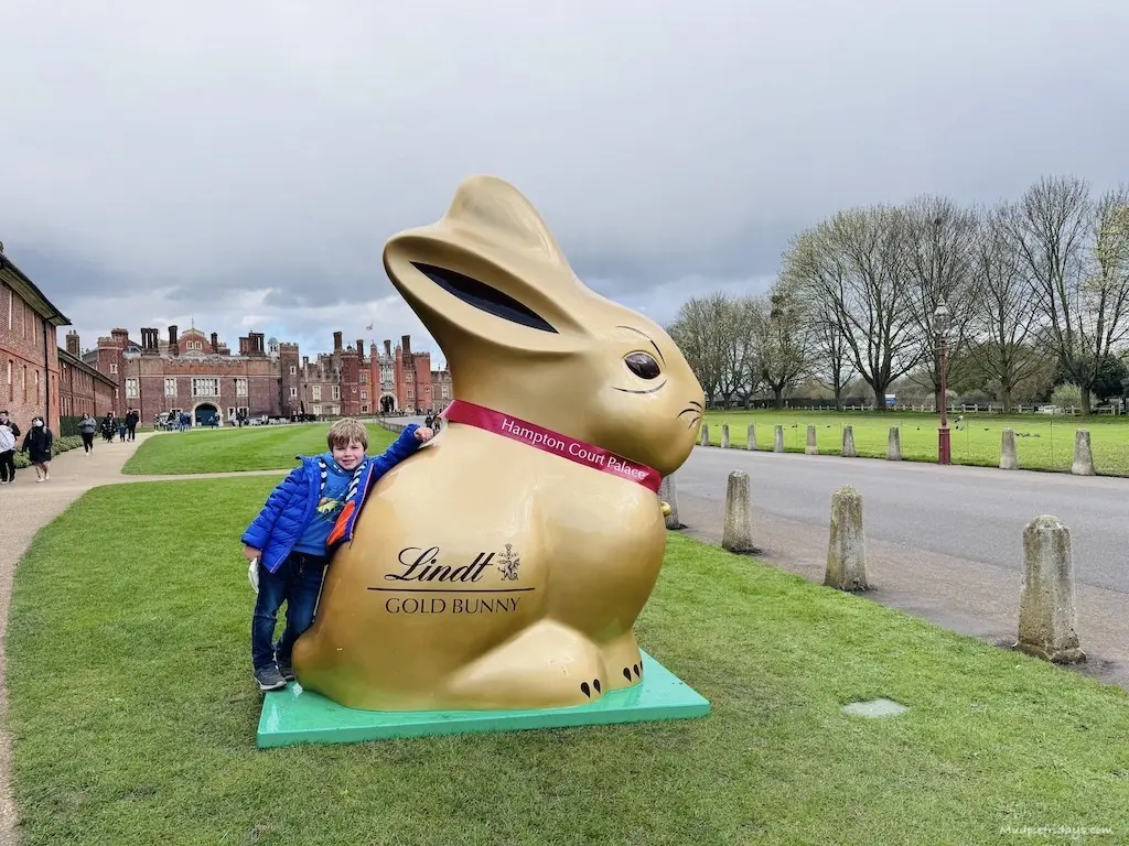 Harry standing with a giant gold bunny outside the front of Hampton Court Palace