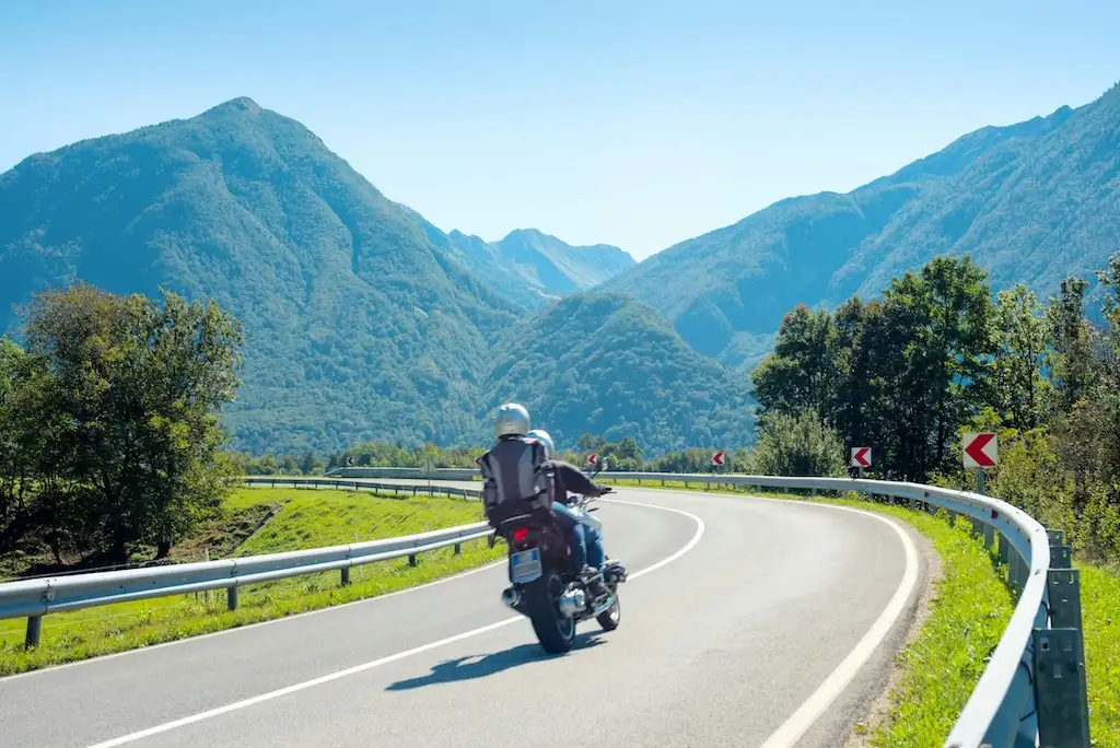 A two-wheeled road trip can turn a familiar stretch of countryside into a proper adventure. You travel close to the landscape, notice the change in temperature as the road climbs and can stop easily when a village café or coastal viewpoint catches your eye. Longer rides do require preparation, though, especially when you’re crossing borders or spending several days away from home. A sensible route, suitable clothing and a well-checked bike will leave you free to enjoy each mile. The Freedom of the Open Road Travelling on two wheels gives you a strong connection to the places you pass through. Smaller roads lead through villages, forests and mountain valleys that can feel distant from busy dual carriageways. Even a short detour may reveal a quiet beach, a family-run bakery or a viewpoint that doesn’t appear in the usual travel guides. That sense of flexibility sits at the heart of many open-road adventures. You can adjust the day around the weather, local events and your energy levels. If a planned mountain route is covered in low cloud, for example, you might follow a lower road and return another day. Freedom still works best within a clear framework. Set a realistic destination for each day and identify several possible stops along the way. This keeps the trip relaxed without leaving you searching for accommodation after dark. Think carefully about the roads you’ll enjoy too. A sweeping coastal route may be memorable, but constant bends and strong crosswinds can make progress slower than expected. A mix of scenic roads and straightforward connecting sections usually creates a more comfortable itinerary. Aim to finish riding well before sunset, giving yourself time to check in, eat and look over the bike before the following morning. Planning Your Journey Start by deciding how many hours you’re comfortable riding in one day. Distance alone can be misleading. Covering 250 kilometres on an open main road may feel manageable, whilst the same distance through mountain passes could take most of the day. Build in a break every 90 minutes or so, even if you don’t yet feel tired. Mark fuel stops, food options and overnight accommodation before leaving. In remote regions, filling stations may close early or operate only on certain days. Download offline maps as a backup because mobile coverage can disappear quickly in valleys and rural areas. Share your route and expected arrival times with someone at home as well. Administrative checks belong near the top of the list. Confirm that your driving documents remain valid for the full trip and review any requirements for the countries you plan to visit. Motorbike owners should also check that their bike insurance provides suitable cover for the proposed route and type of bike. Keep digital and paper copies of relevant documents in separate places. For a longer international route, guides can offer useful ideas about pacing and destinations. Treat suggested itineraries as starting points, then adjust them to your own experience and available time. An extra night in one location often gives you a valuable rest day if the weather turns or the route takes longer than planned. Essential Gear for Longer Rides Pack for protection, comfort and changing conditions. A properly fitted helmet, protective jacket, trousers, gloves and boots form the foundation of your riding kit. Check that everything remains comfortable after several hours, as a collar or seam that feels slightly awkward at home can become distracting during a full day on the road. Layering works well when temperatures vary. A thin base layer, warm mid-layer and waterproof outer clothing take up less space than several bulky items. Keep waterproofs somewhere accessible instead of at the bottom of a tightly packed bag. Weather can change within minutes on exposed roads, and stopping early gives you time to add a layer safely. Useful items for a longer trip include: A small first-aid kit and any personal medicines Water and a few high-energy snacks A tyre pressure gauge and compact repair supplies Charging cables and a portable power bank A high-visibility layer for poor weather Ear protection designed for road use A secure lock and waterproof document pouch Spread the load evenly and secure every bag according to its manufacturer’s instructions. Loose straps can flap in the wind or move towards hot and rotating parts. Put heavier items low and close to the centre of the bike, then take a brief test ride before departure. If the steering or balance feels different, stop and repack. Resist filling every available space. Lighter luggage makes the bike easier to handle and leaves room for food, souvenirs or an extra layer picked up during the trip. Ensuring a Smooth Trip Give the bike a thorough check several days before leaving, which allows time to deal with any faults. Inspect tyre condition and pressure, lights, mirrors, fluid levels, brakes and the drive system. Follow the maintenance guidance in the owner’s manual and arrange professional help if anything seems unusual. Repeat a shorter inspection each morning. Look for fresh leaks, loose luggage or visible tyre damage, then test the lights and controls before setting off. This routine takes only a few minutes and may identify a small issue before it disrupts the day. Your own condition matters just as much. Dehydration, poor sleep and hunger can reduce concentration, so drink water regularly and eat before you feel drained. Stop if your attention begins to wander or you find yourself reacting late to bends and signs. A 20-minute break in a safe location is more useful than pressing on to meet an arbitrary arrival time. Conditions on the day should guide your decisions. Heavy rain, high winds or extreme heat may call for a shorter route or an unplanned overnight stop. Keep one flexible day in the schedule for longer trips. It can absorb a mechanical delay, provide recovery time or let you stay somewhere that deserves more than a quick visit. That single unscheduled day often prevents the rest of the holiday from feeling rushed. Adventures Beyond the Usual Popular routes earn their reputation, but memorable trips often include less obvious places between the headline attractions. Look beyond major cities and search for national parks, heritage railways, local markets and small museums. Routes such as a Basque Country road trip show how coastal roads, smaller towns and scenic detours can become just as memorable as the main destinations. The love of the open road often comes from these unplanned discoveries and the changing scenery between them. Castles can also provide useful focal points for a route. They tend to be located in historically significant towns or dramatic rural settings, with cafés, walking trails and other attractions nearby. Once you arrive, give yourself time away from the bike. A short walk through a historic centre or along a coastal path helps loosen tired muscles and lets you experience more than the road itself. Booking two nights in one place can work particularly well on longer tours, creating space for a local loop without carrying all your luggage. Respect local communities as you travel. Use marked parking areas, keep noise low near homes and follow access rules in protected landscapes. Spending money in independent cafés, shops and accommodation also helps the places that make these routes rewarding. The best final evening is one with no frantic dash to reach the ferry, train or front door. Leave a generous margin for the homeward leg, choose an enjoyable last stretch and let the trip finish at the same measured pace at which it began.